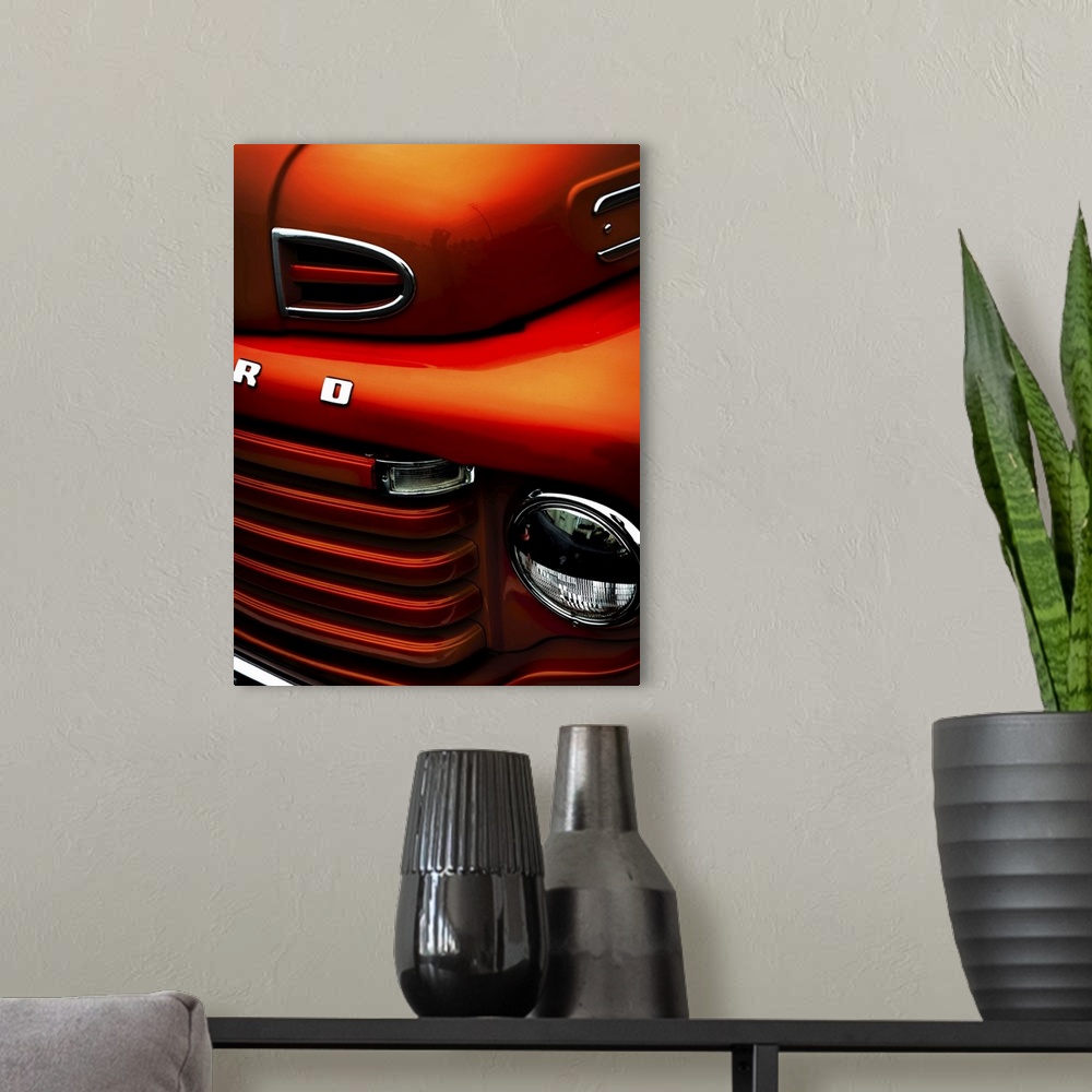 A modern room featuring The headlight and front grille of a fiery orange vintage ford truck.