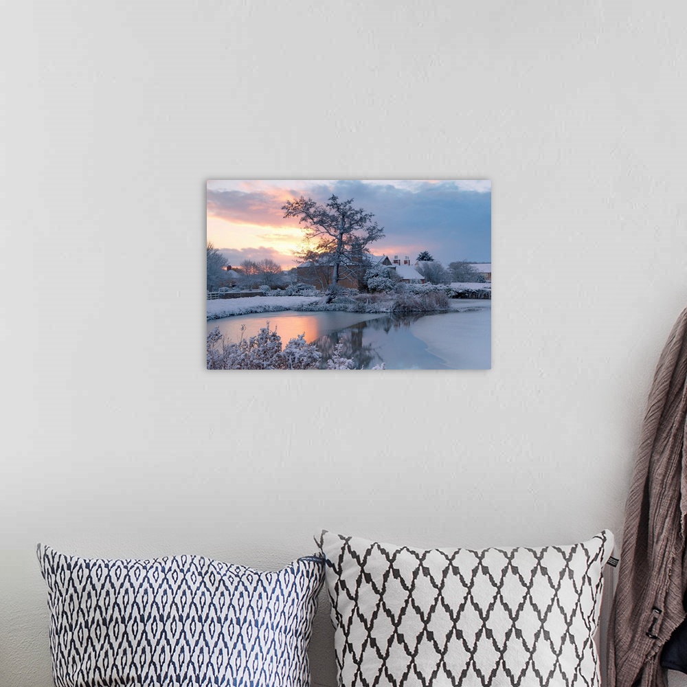 A bohemian room featuring A golden dawn over a village pond and snowy fields to the village roofs beyond with trees in snow...
