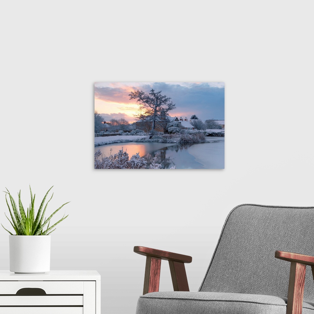 A modern room featuring A golden dawn over a village pond and snowy fields to the village roofs beyond with trees in snow...