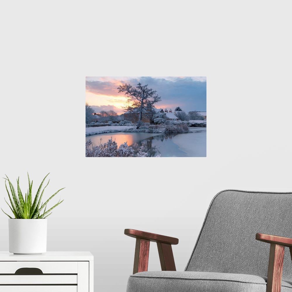 A modern room featuring A golden dawn over a village pond and snowy fields to the village roofs beyond with trees in snow...