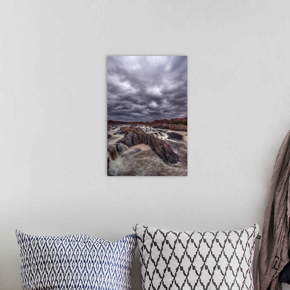 A bohemian room featuring Very dark storm clouds over a rushing river lined with rocks.