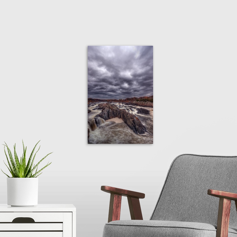 A modern room featuring Very dark storm clouds over a rushing river lined with rocks.