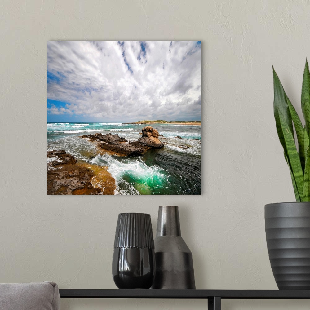 A modern room featuring Photograph of rocky surf on a very cloudy day. A small hilly beach is in the distance.