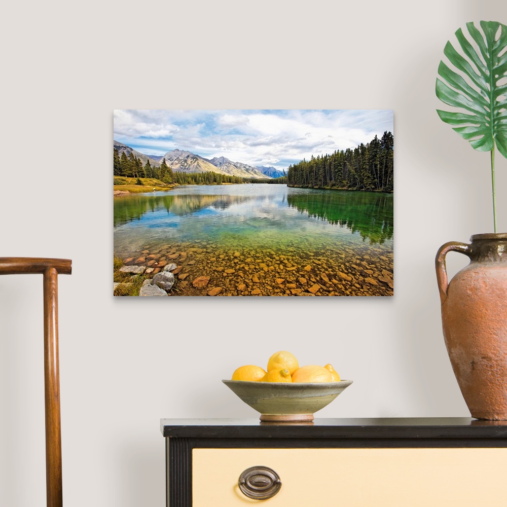A traditional room featuring Giant photograph taken from the rocky shores of a lake that is surrounded by dense forests and sn...