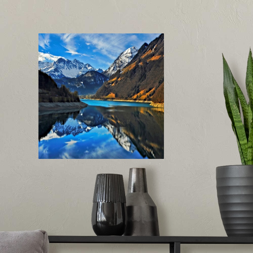A modern room featuring Square photograph on a big wall hanging of snow covered mountains beneath a blue sky, reflecting ...