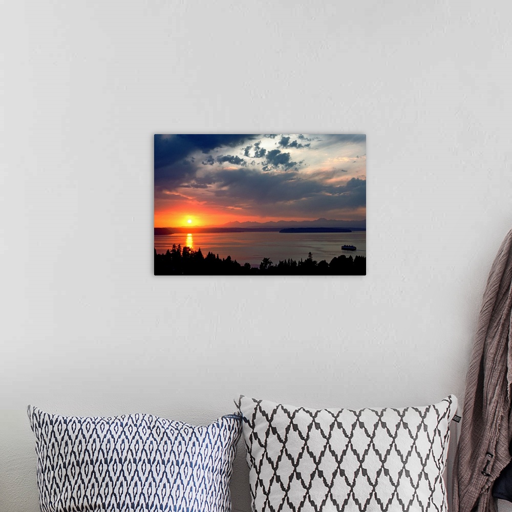A bohemian room featuring Horizontal photograph of a vibrant setting sun in a partly cloudy sky, over a large body of water...