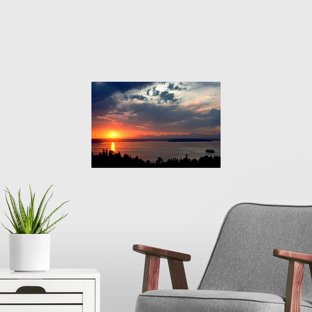 A modern room featuring Horizontal photograph of a vibrant setting sun in a partly cloudy sky, over a large body of water...