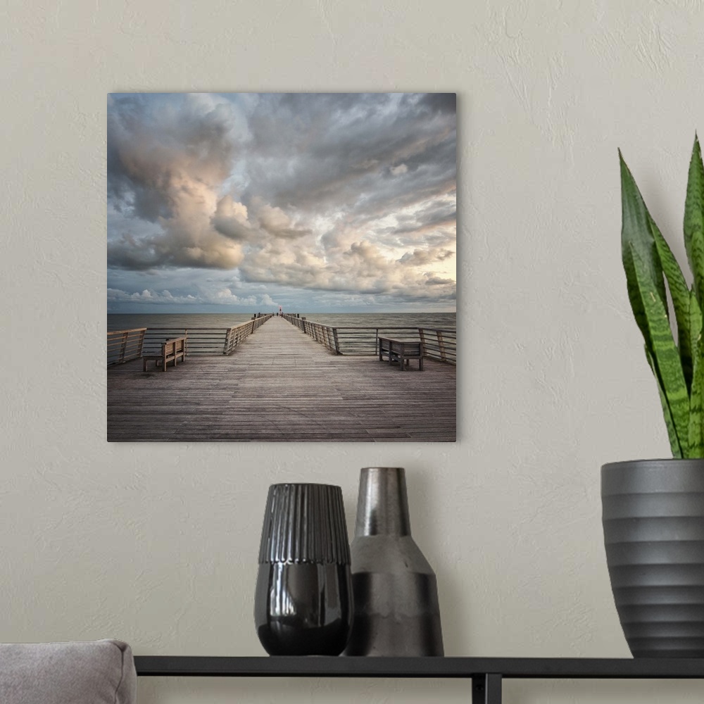 A modern room featuring A wooden pier leading to the ocean with dramatic clouds above.