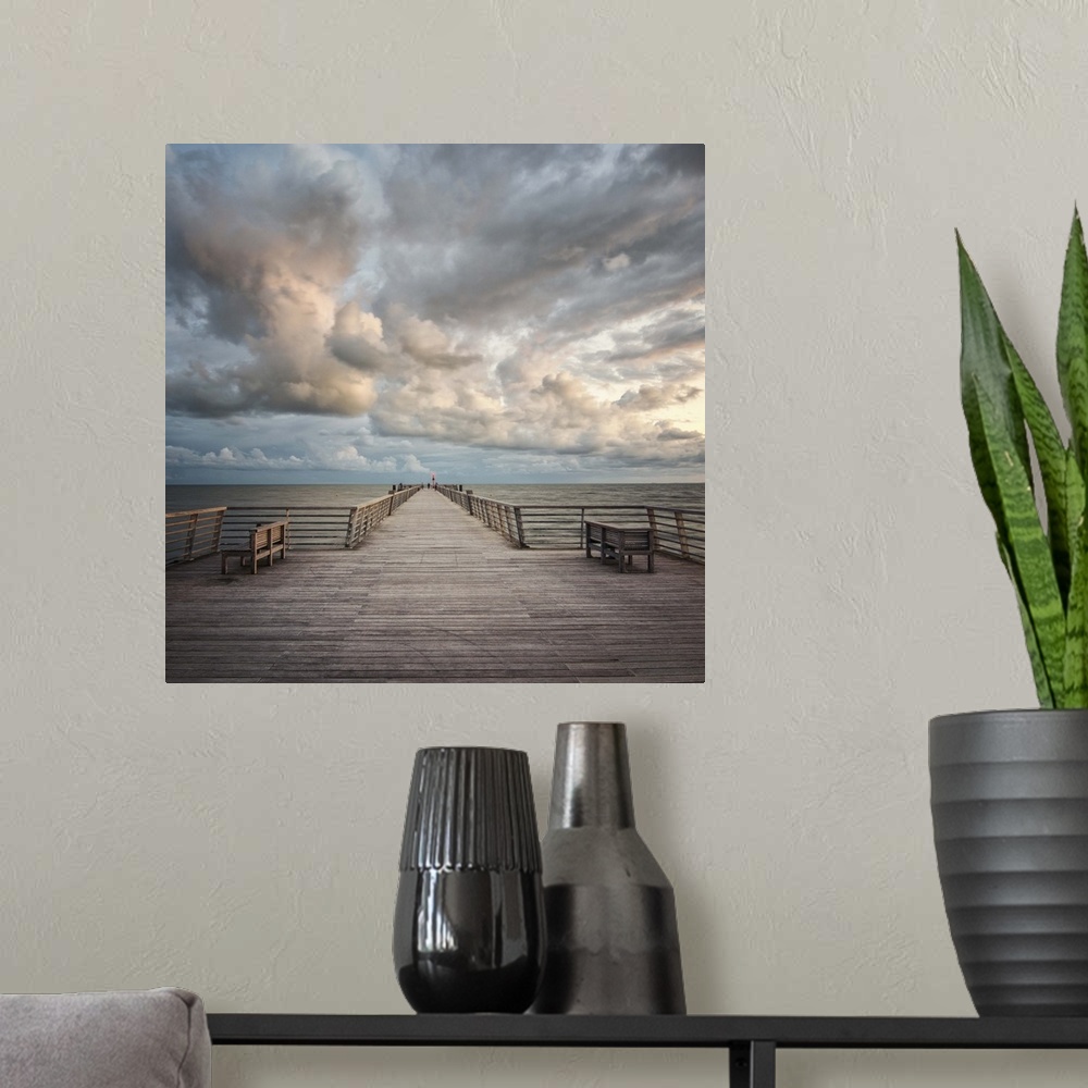 A modern room featuring A wooden pier leading to the ocean with dramatic clouds above.