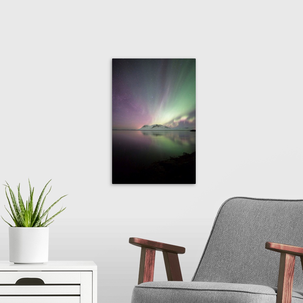 A modern room featuring Green and purple northern lights over the ocean and mountains in Iceland at night.