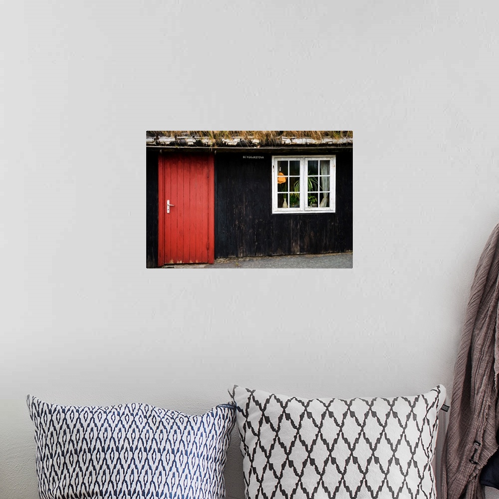 A bohemian room featuring A black painted house with a bright red door and a white window.