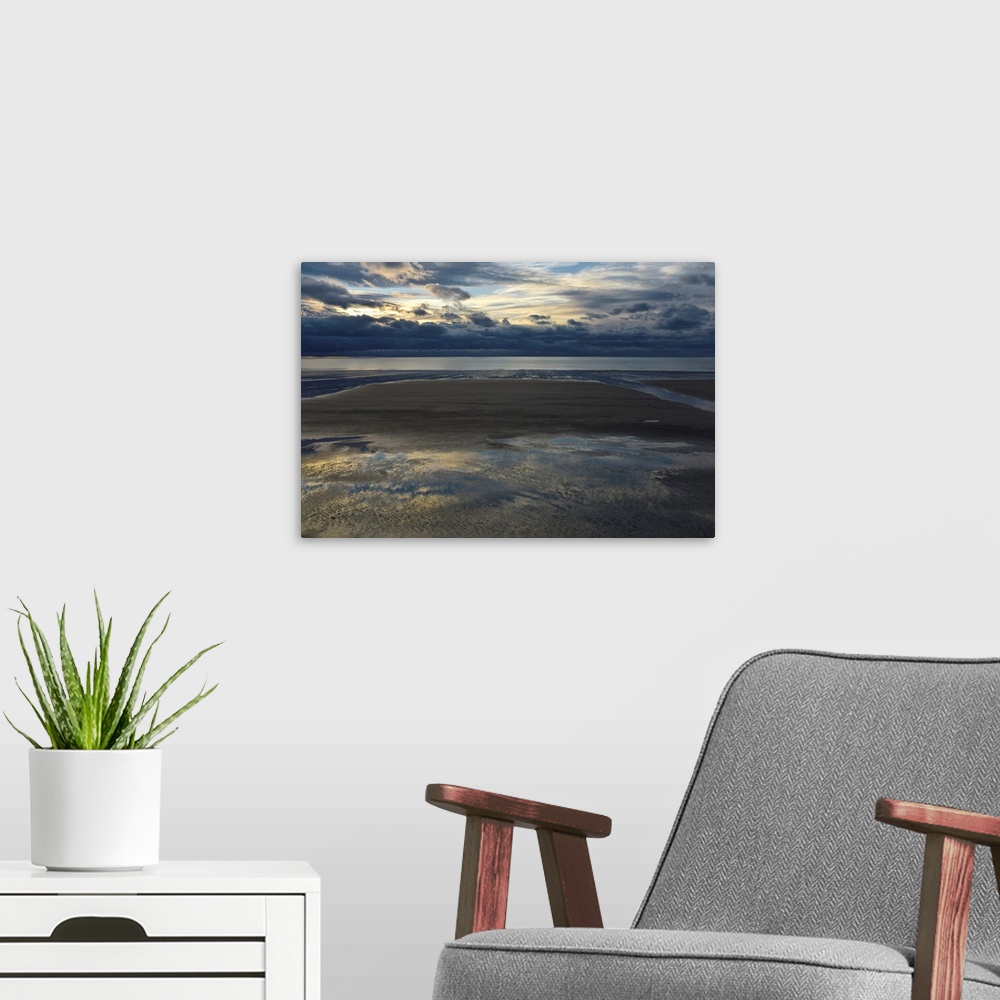 A modern room featuring Landscape photograph of an empty beach on a cloudy day with the sky reflecting onto the puddles i...
