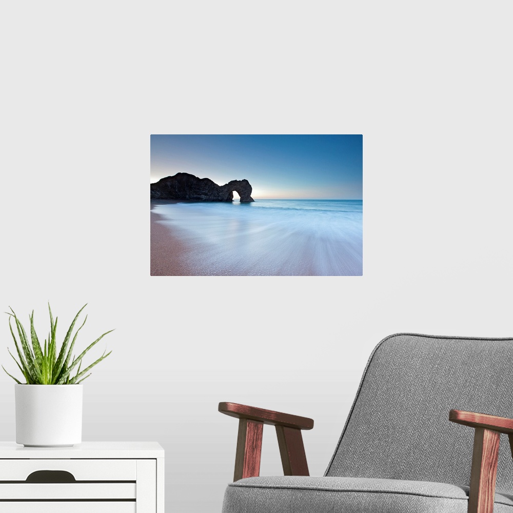 A modern room featuring Durdle Door rock arch on the Dorset coast at sunrise with a blue sky and swooshing waves in minim...