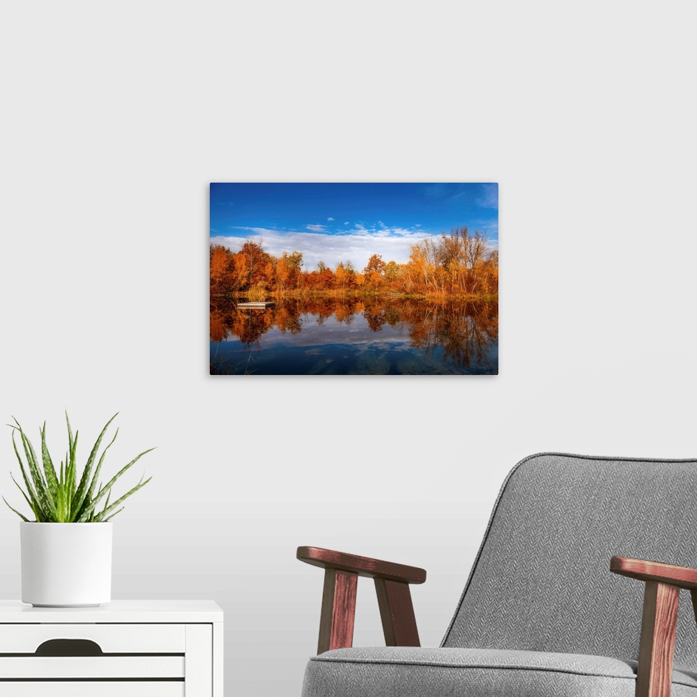 A modern room featuring Autumn scenery around a lake under a beautiful blue sky