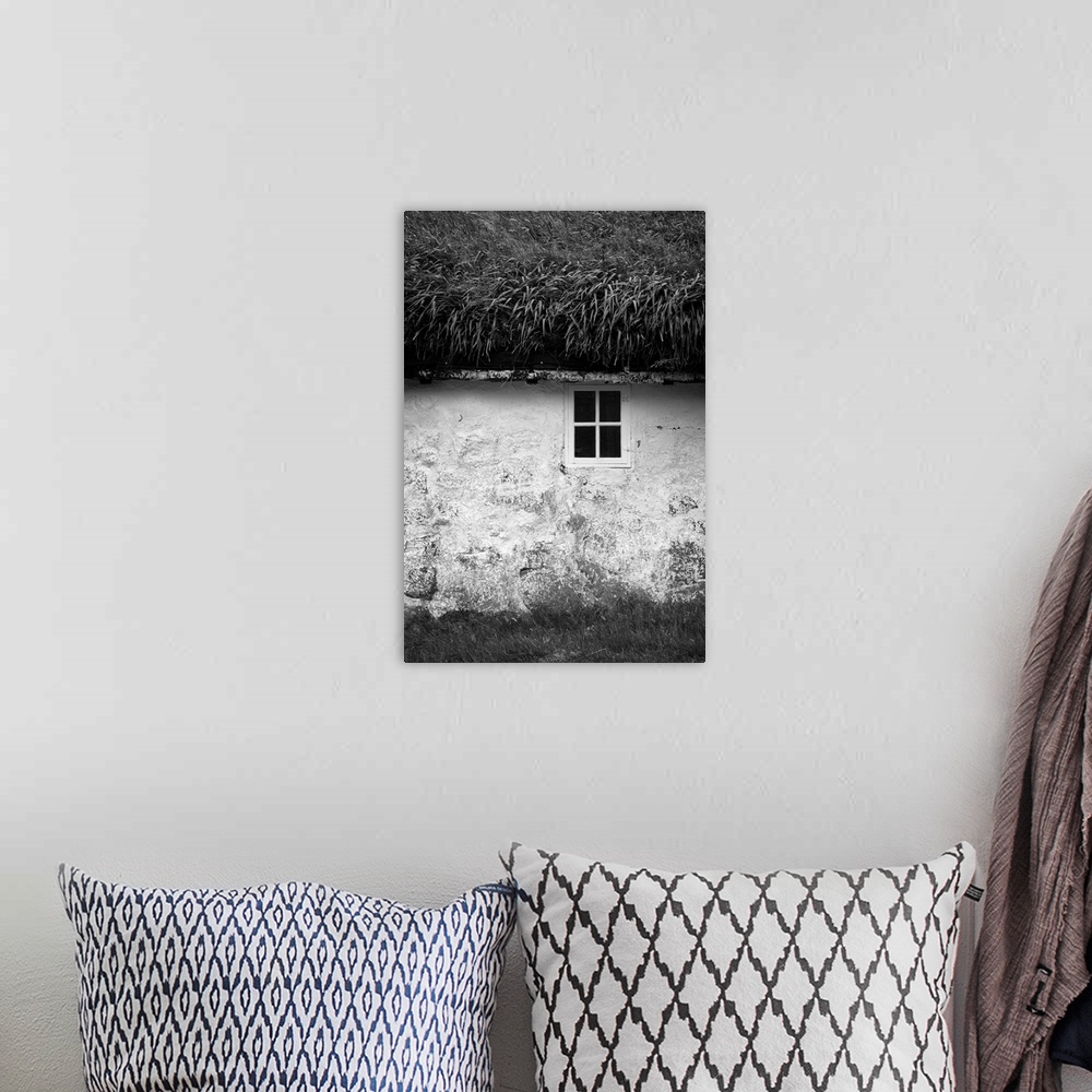 A bohemian room featuring Black and white image of a small window in the stone wall of a house with a grassy roof.