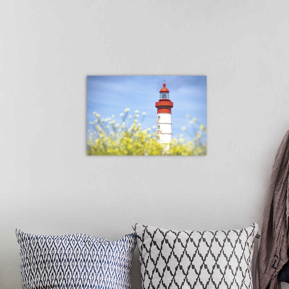 A bohemian room featuring Saint Mathieu lighthouse under a blue sky and behind yellow flowers in Plougonvelin, France.