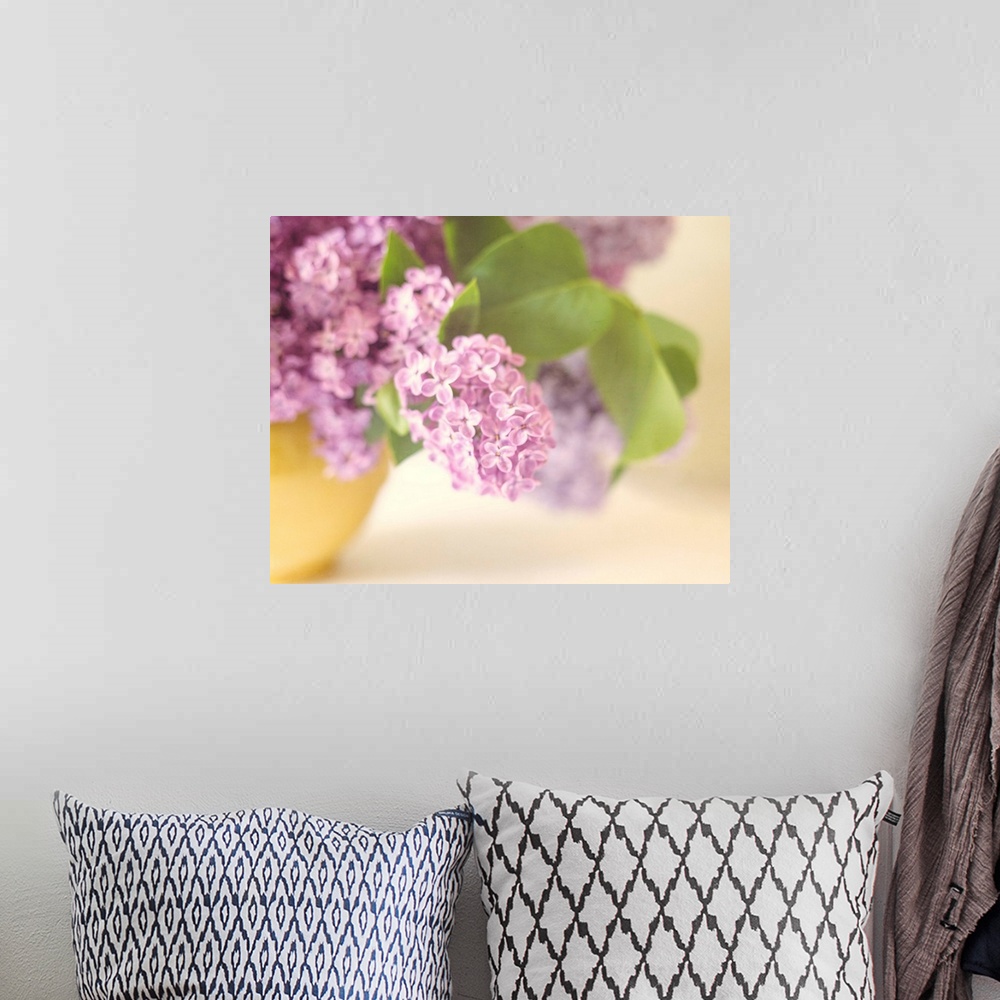 A bohemian room featuring A soft focus vintage bowl of Lilac flower blossoms in a soft yellow vase.