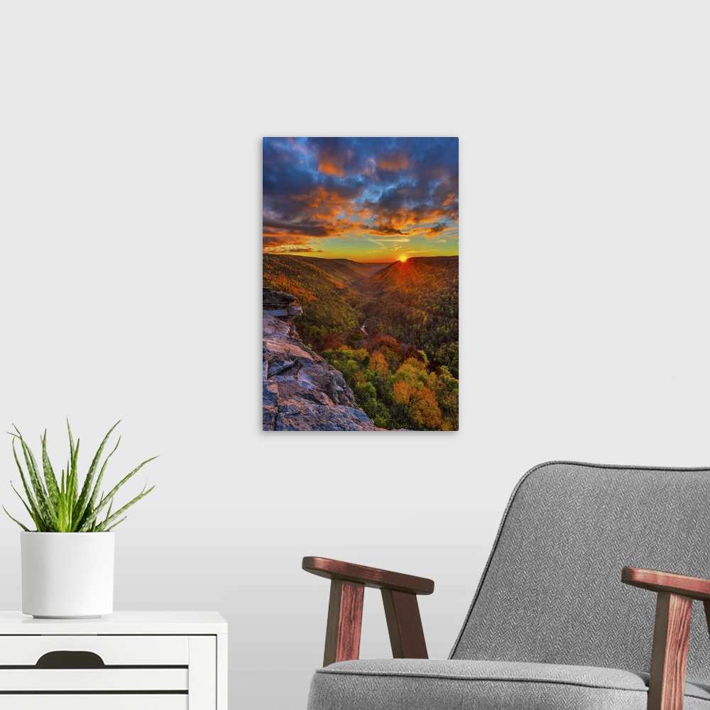 A modern room featuring The sun on the horizon casting a vivid glow in the clouds over a dense forest in West Virginia.
