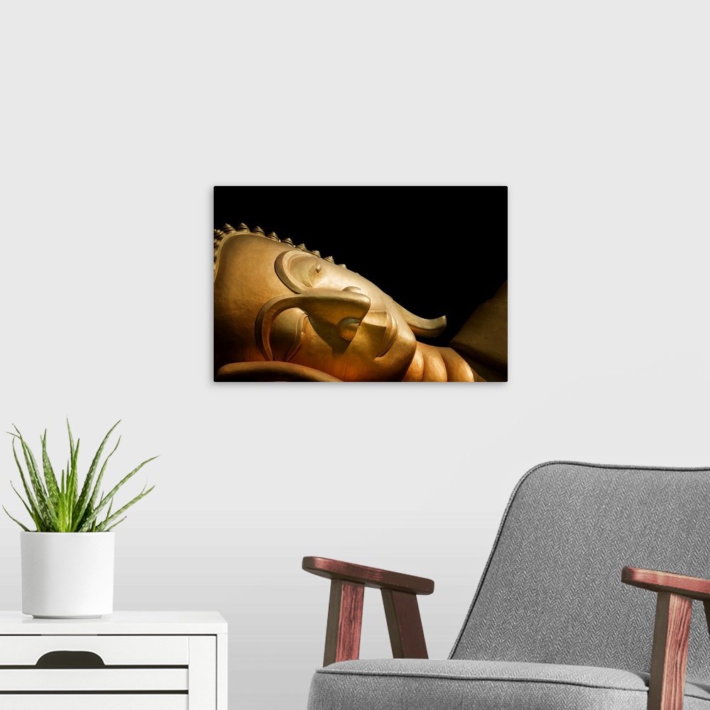 A modern room featuring The head of a reclining Buddha in front of a black background