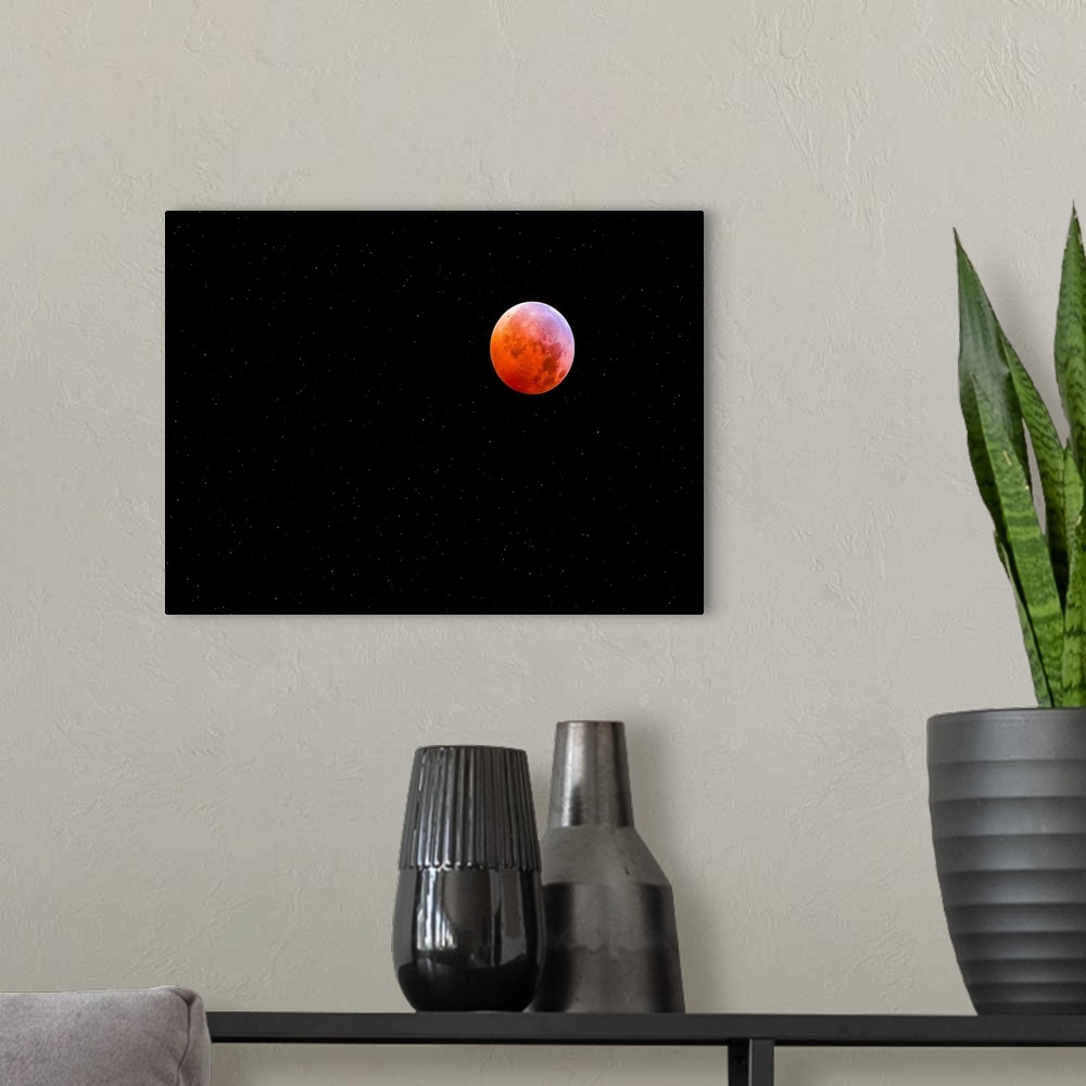 A modern room featuring The moon in a starry night sky glowing bright red during an eclipse.