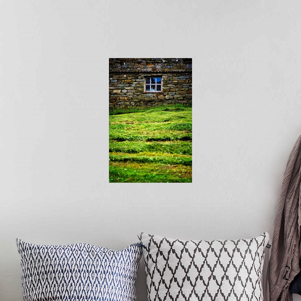 A bohemian room featuring Photograph taken of a stone wall with a window in it and thick cut grass just in front.