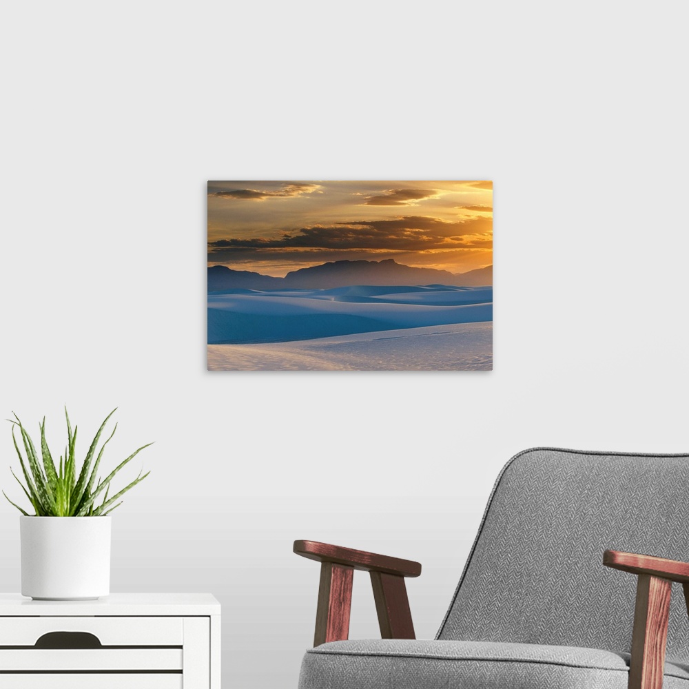 A modern room featuring Large landscape photograph of the sun setting in a cloudy sky, over the Gypsum dunes, White Sands...