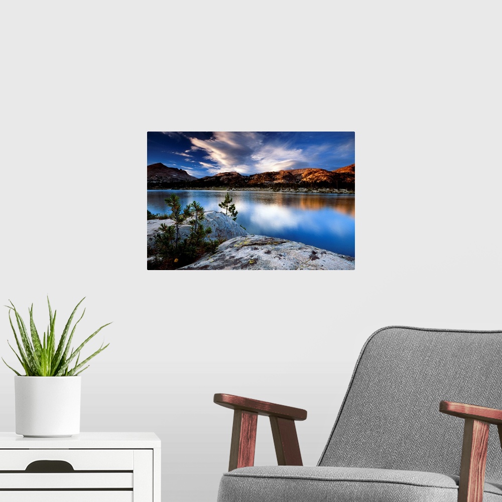 A modern room featuring Sunset lit clouds hover over a mountain range that is photographed from across a body of water wi...