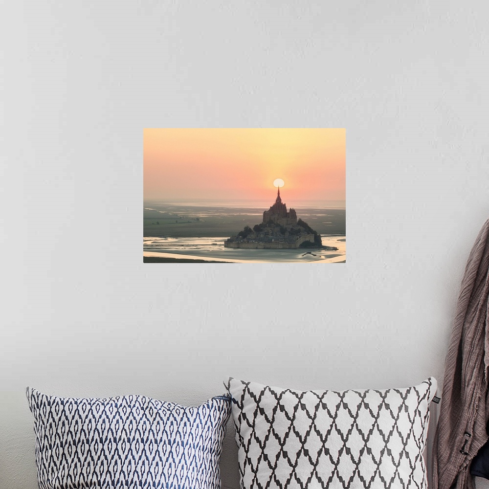 A bohemian room featuring The sun appearing to rest on the spire at the top of Mont Saint Michel in France at sunset.