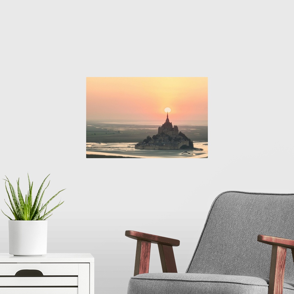A modern room featuring The sun appearing to rest on the spire at the top of Mont Saint Michel in France at sunset.