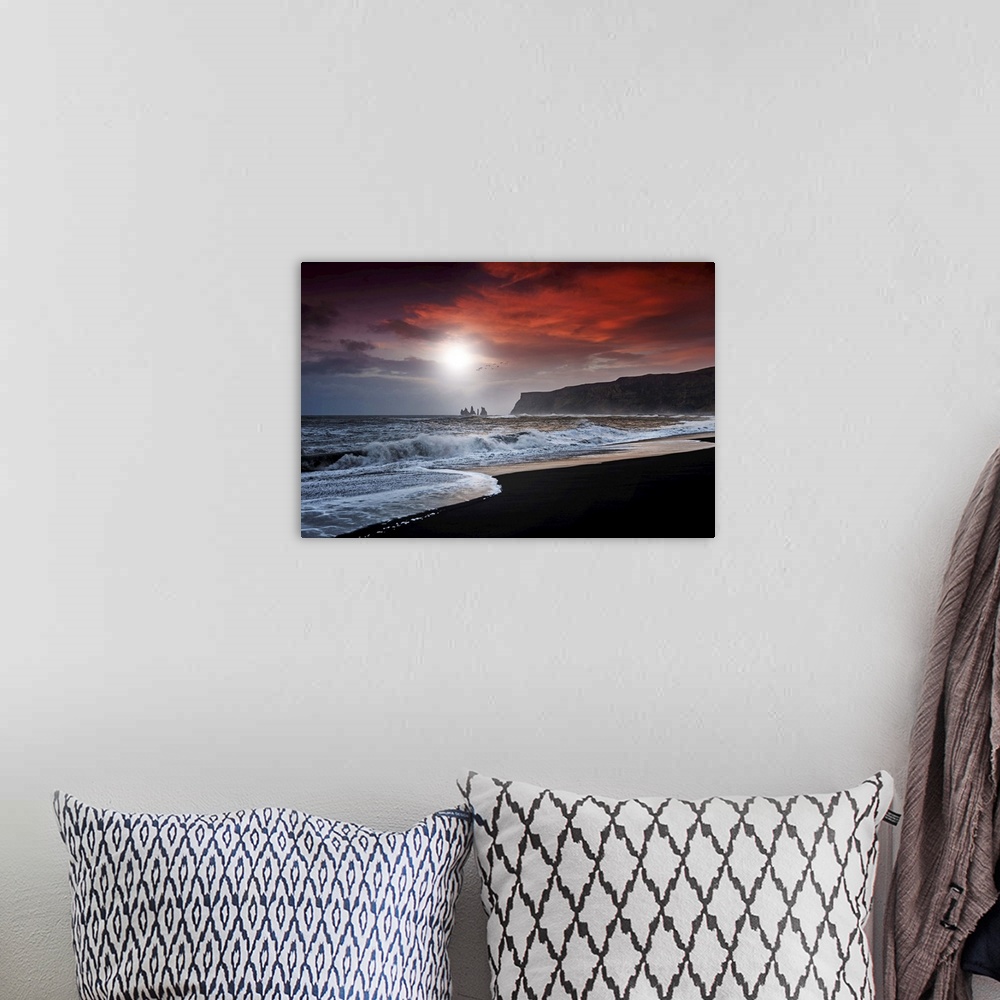 A bohemian room featuring A photograph of a dark coastline under a red clouds.
