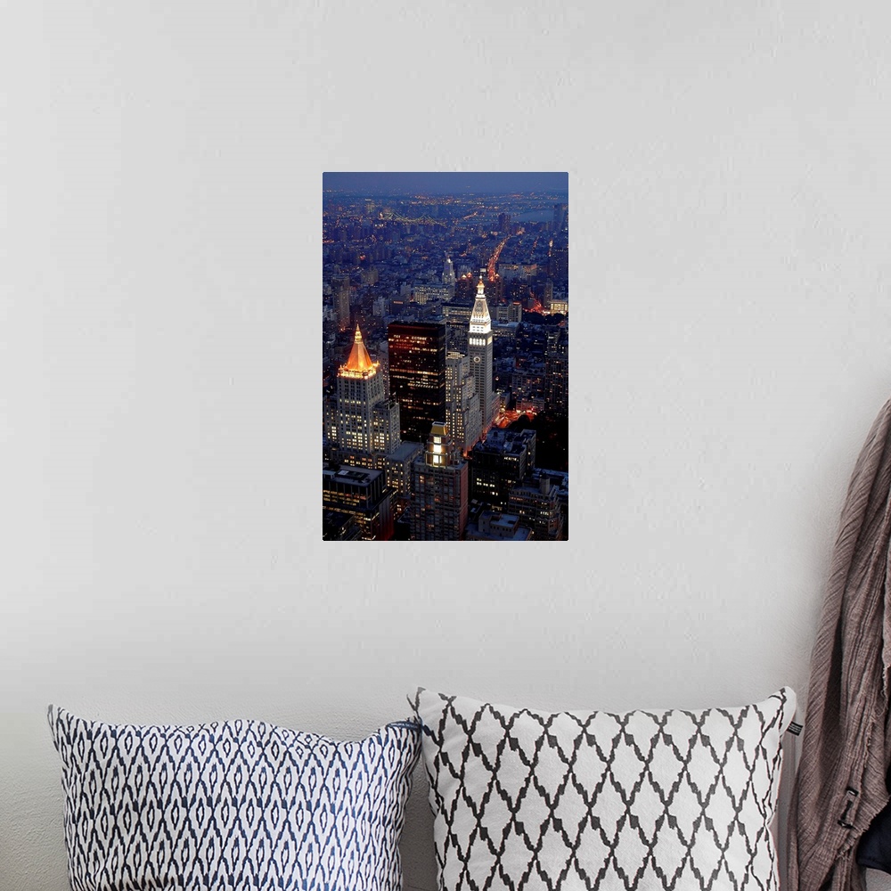 A bohemian room featuring This vertical artwork is an aerial photograph of a Manhattan skyscrapers illuminated in the evening.