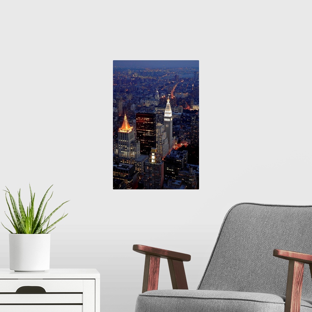 A modern room featuring This vertical artwork is an aerial photograph of a Manhattan skyscrapers illuminated in the evening.