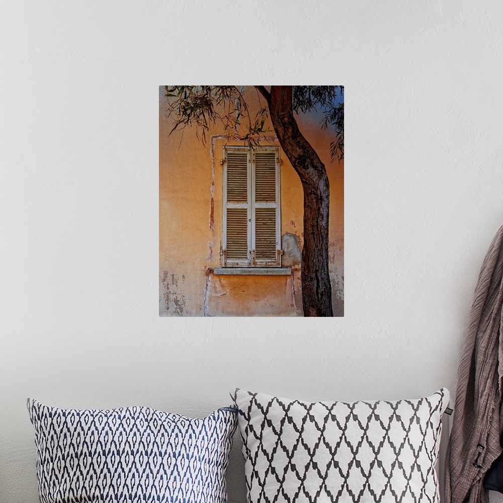 A bohemian room featuring Photograph of an orange building facade with a weathered window with white shutters and a tree in...