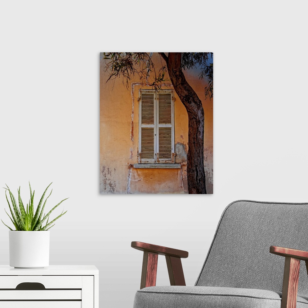 A modern room featuring Photograph of an orange building facade with a weathered window with white shutters and a tree in...