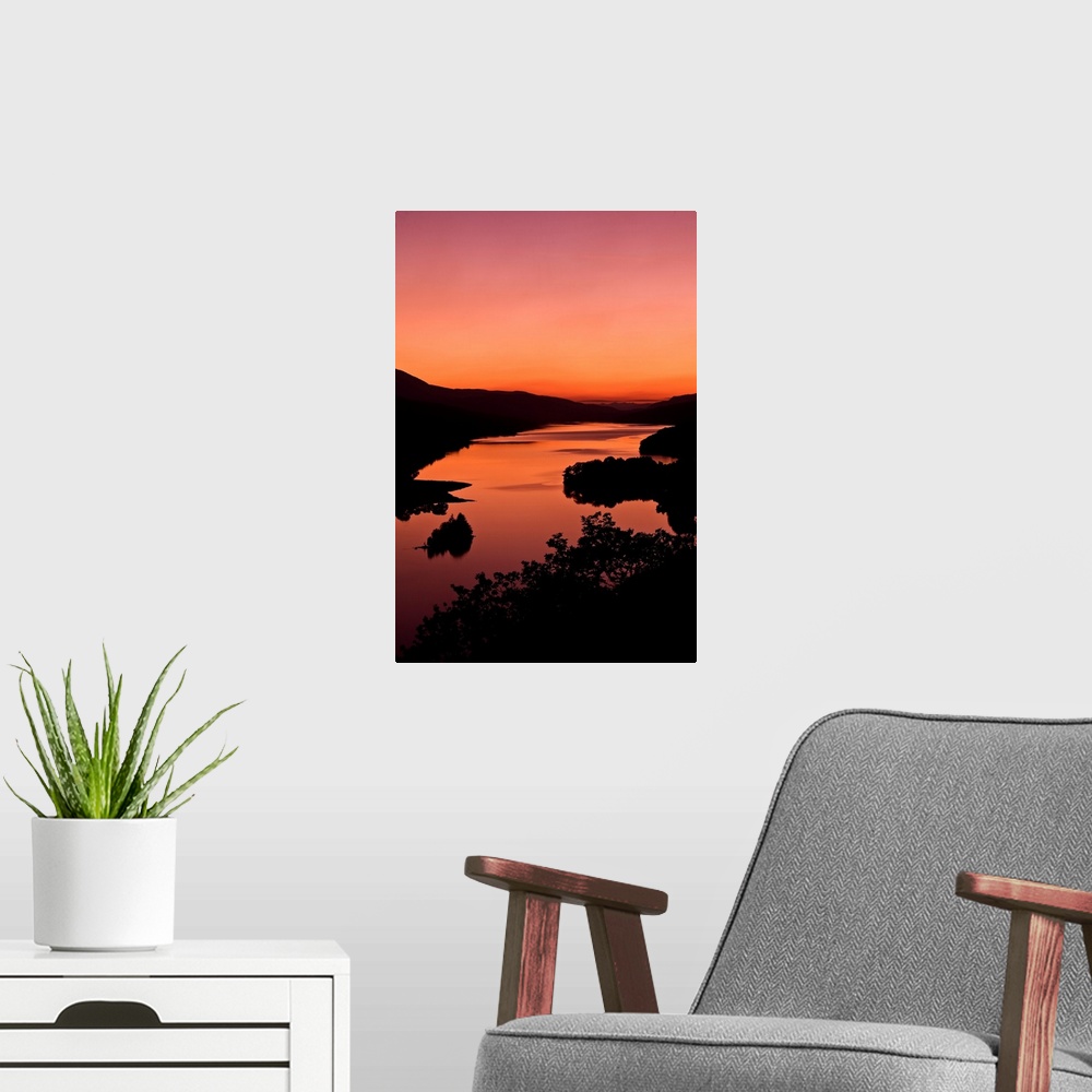 A modern room featuring An intense orange sunset landscape view over a loch in Scotland.