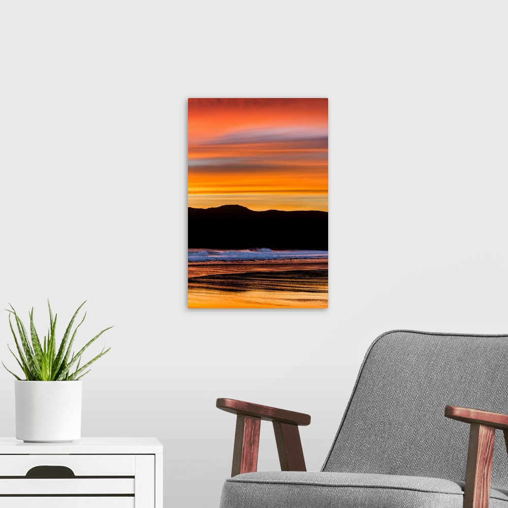 A modern room featuring Vibrant orange clouds reflected in the ocean water at sunset on the pacific coast.