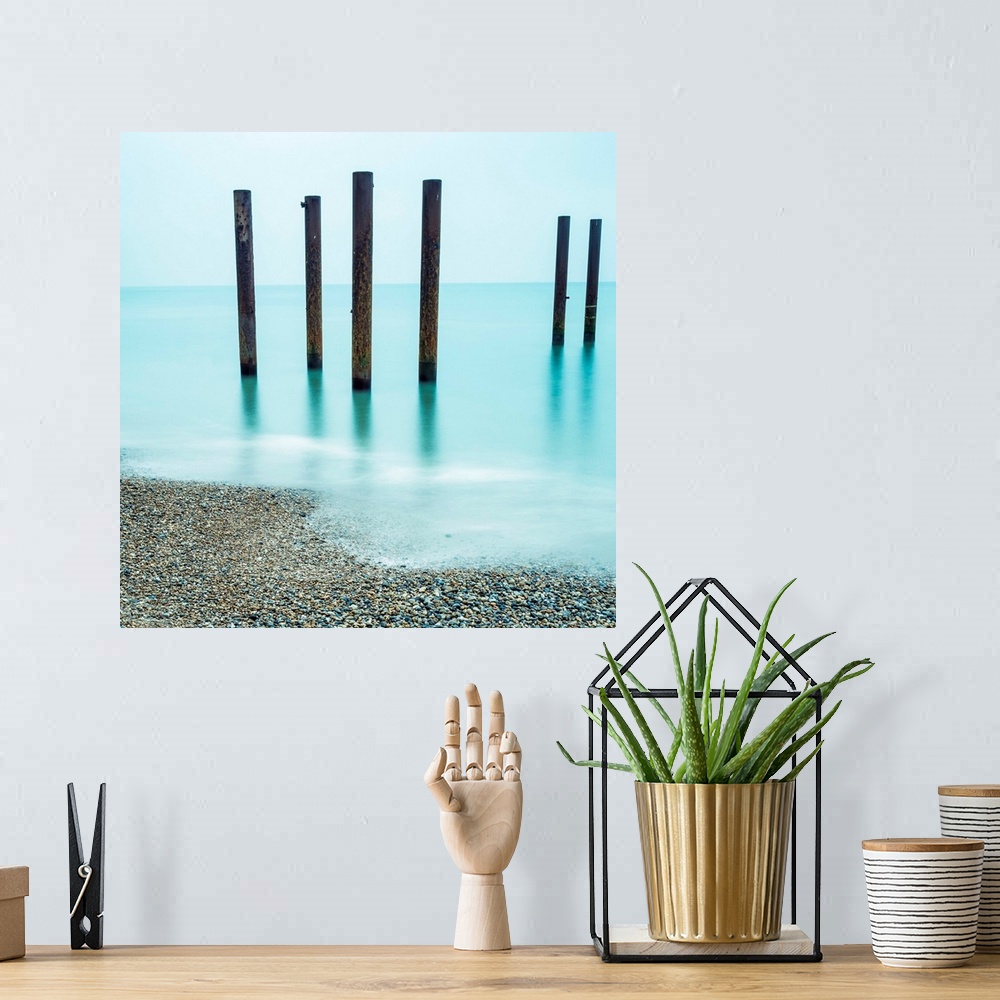 A bohemian room featuring A photograph of wooden poles from a pier sticking up from the water along a beach.