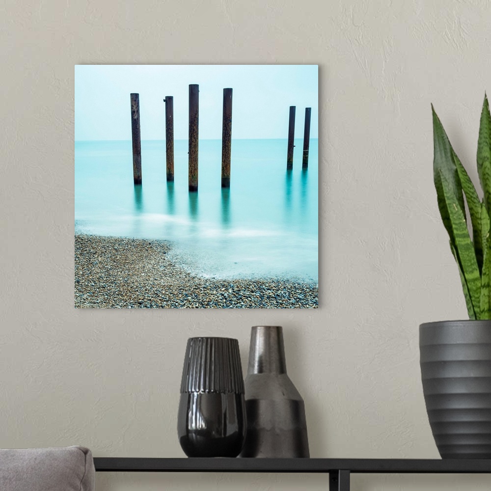 A modern room featuring A photograph of wooden poles from a pier sticking up from the water along a beach.
