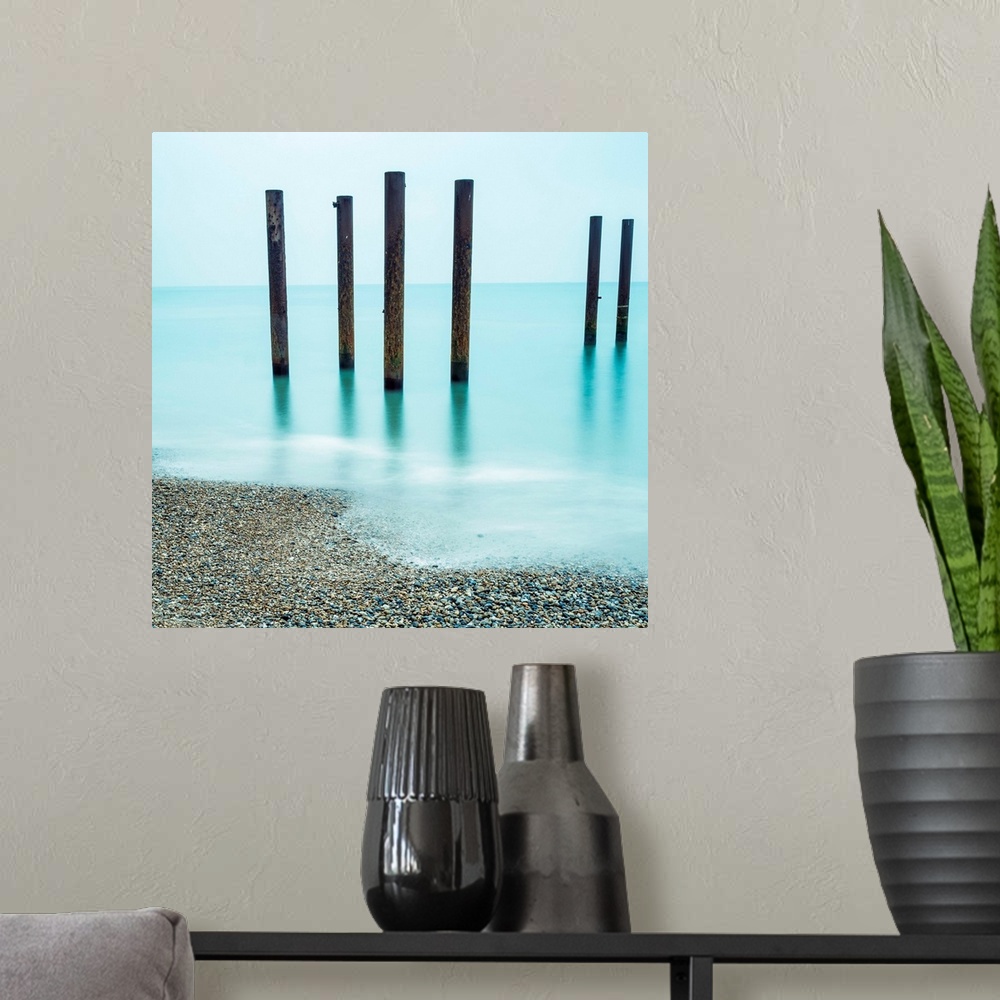 A modern room featuring A photograph of wooden poles from a pier sticking up from the water along a beach.