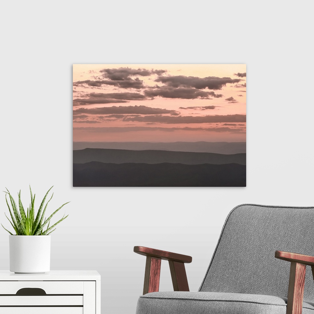 A modern room featuring Pale pink cloudy sky over dark hills at twilight.