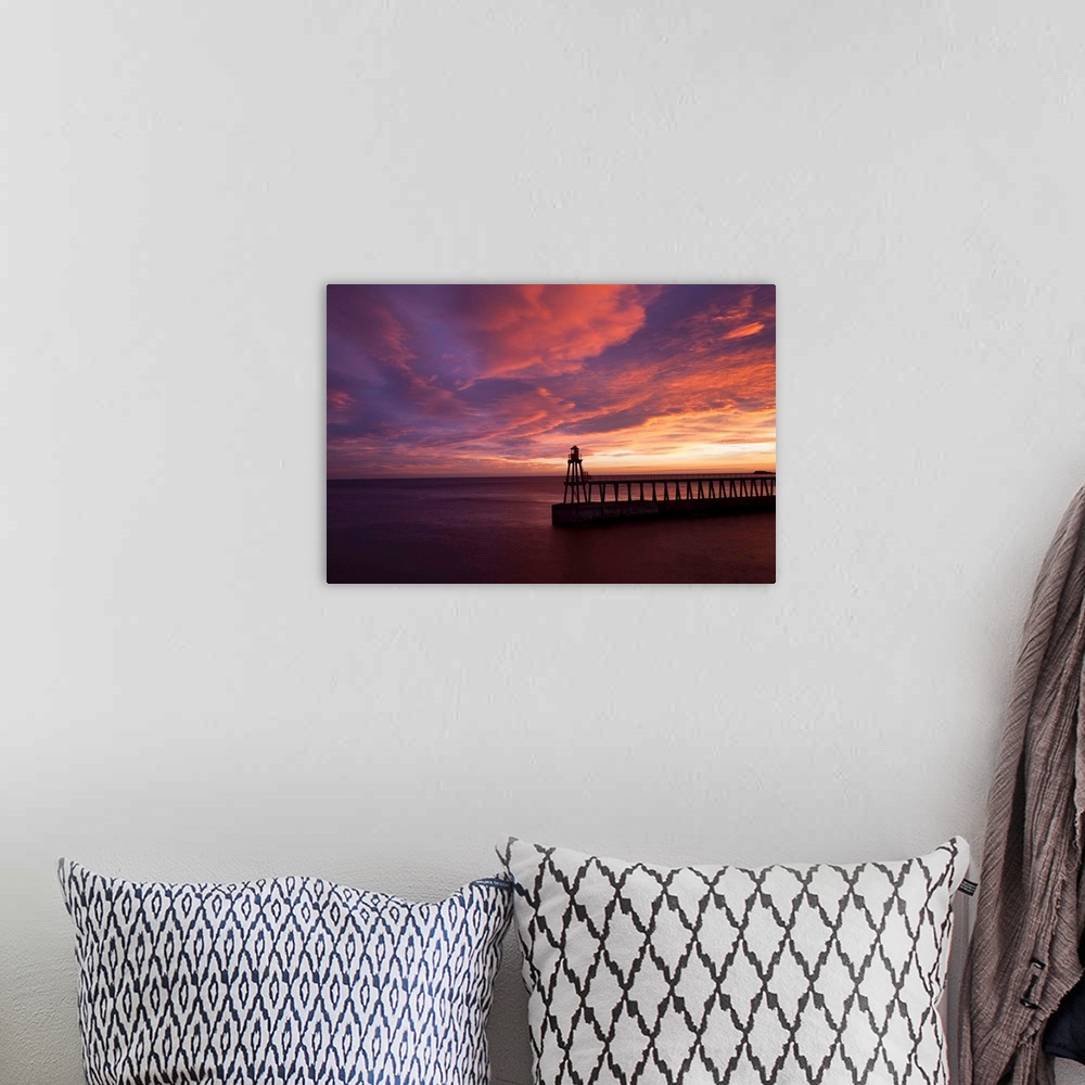 A bohemian room featuring A dramatic peach, orange and red sunset over the lighthouse and pier at Whitby harbour, North Yor...