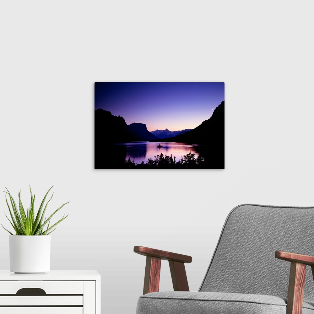 A modern room featuring Mountainous terrain is silhouetted by the sunset and a large body of water sits in between. A sma...
