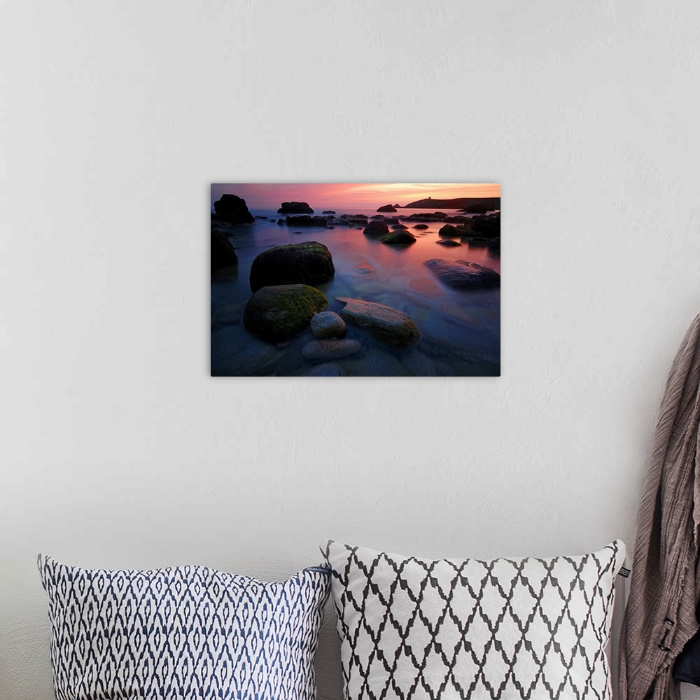 A bohemian room featuring Rocky beach during pink sunset in Brittany, France, big rocks and quite sea at first plan.