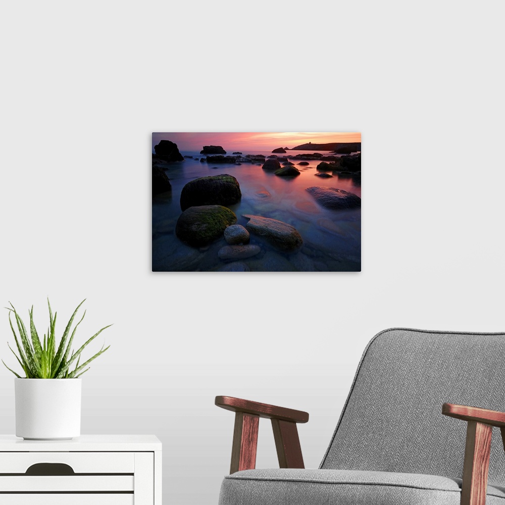A modern room featuring Rocky beach during pink sunset in Brittany, France, big rocks and quite sea at first plan.