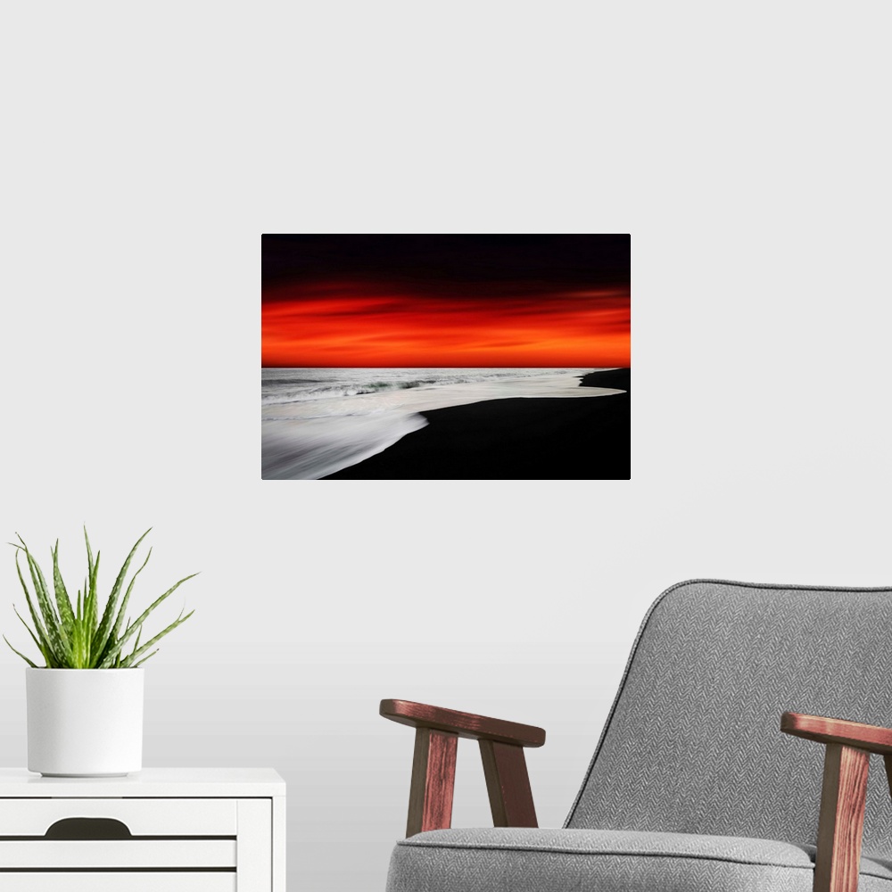 A modern room featuring A dramatic photograph of a blazing sky hanging over a white seascape seen from a black sand beach.