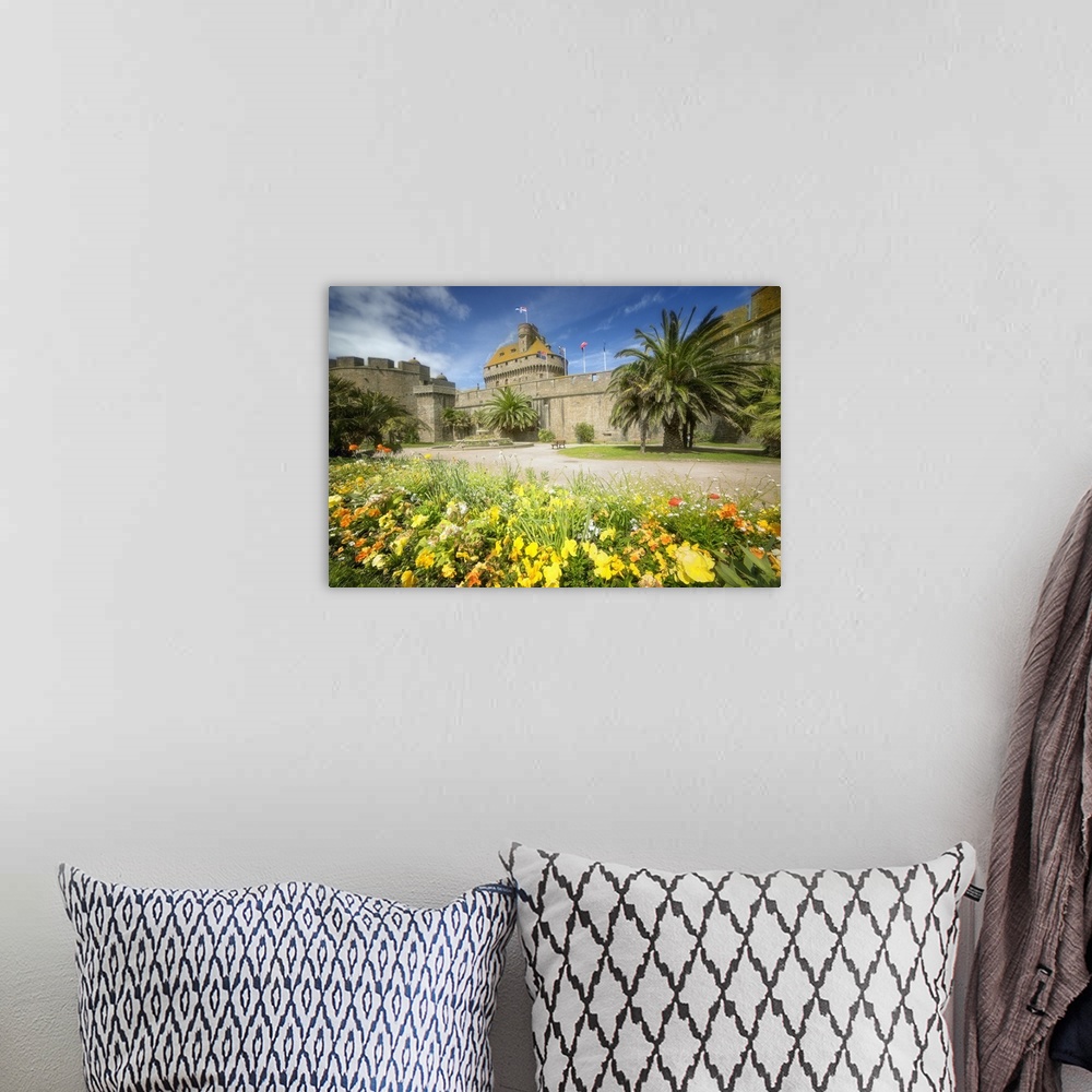 A bohemian room featuring A historic castle in Brittany, France, surrounded by yellow flowers and palm trees.
