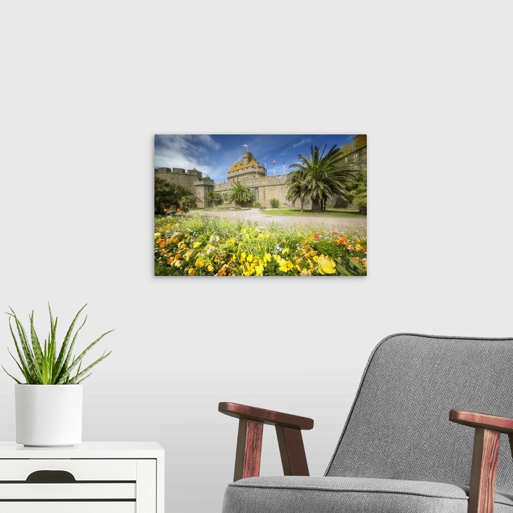 A modern room featuring A historic castle in Brittany, France, surrounded by yellow flowers and palm trees.
