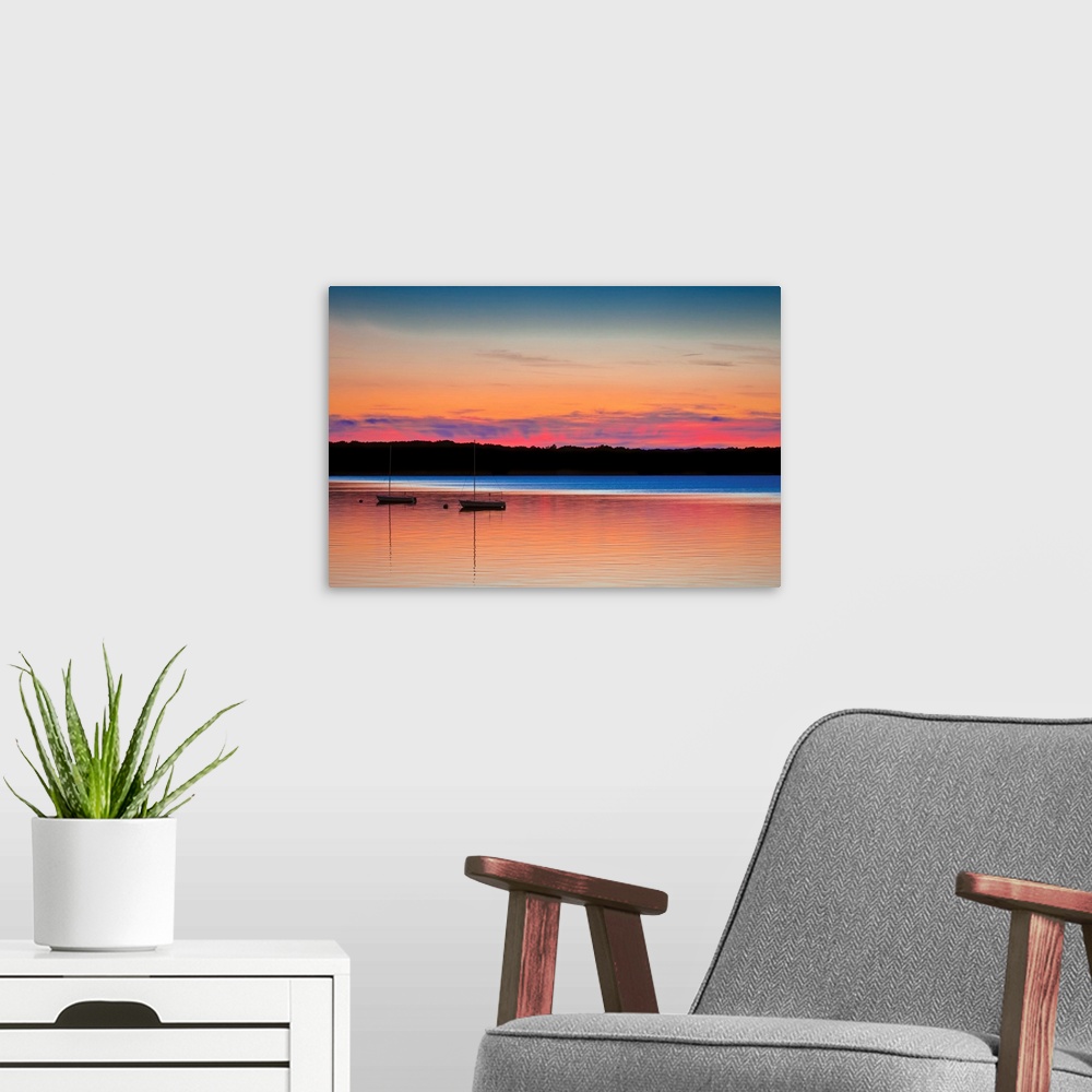 A modern room featuring Two boats on calm waters under a colorful sunset in shades of pink, orange, and blue.