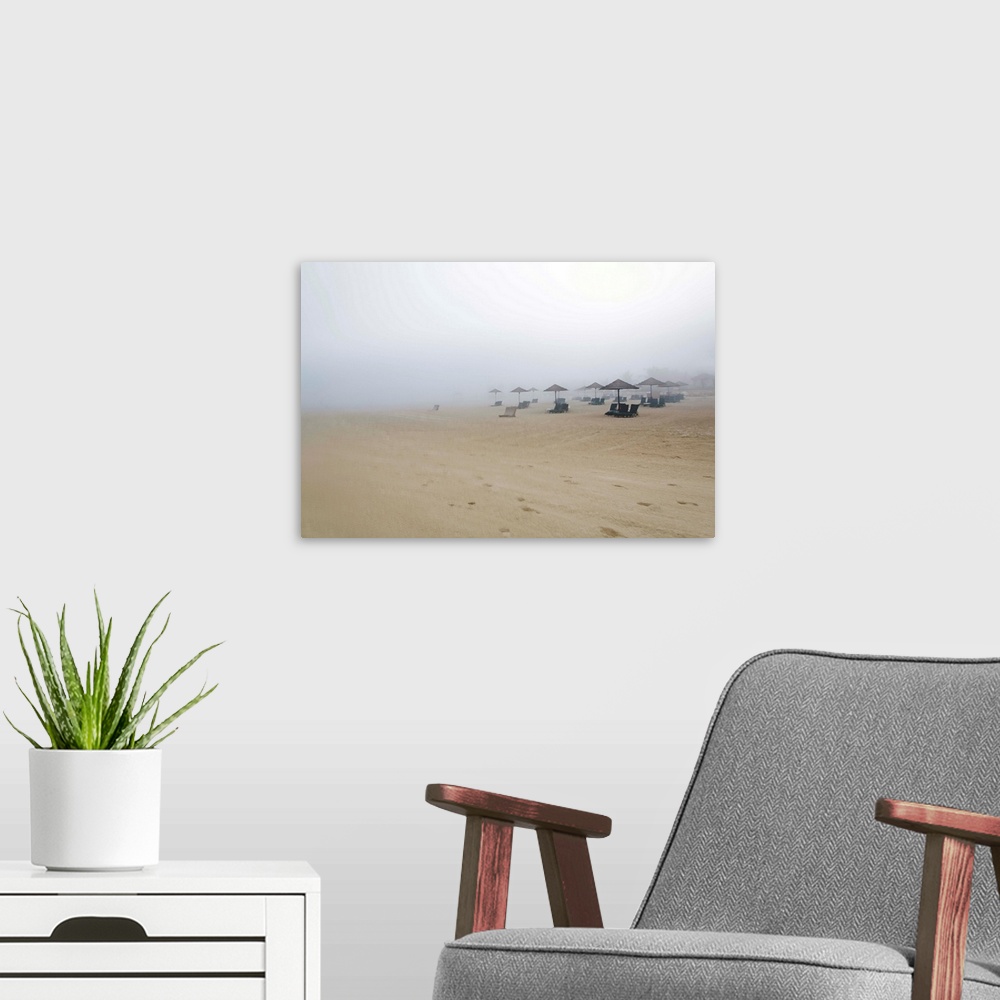 A modern room featuring Landscape photograph of a sandy beach covered in fog and beach chairs with umbrellas.