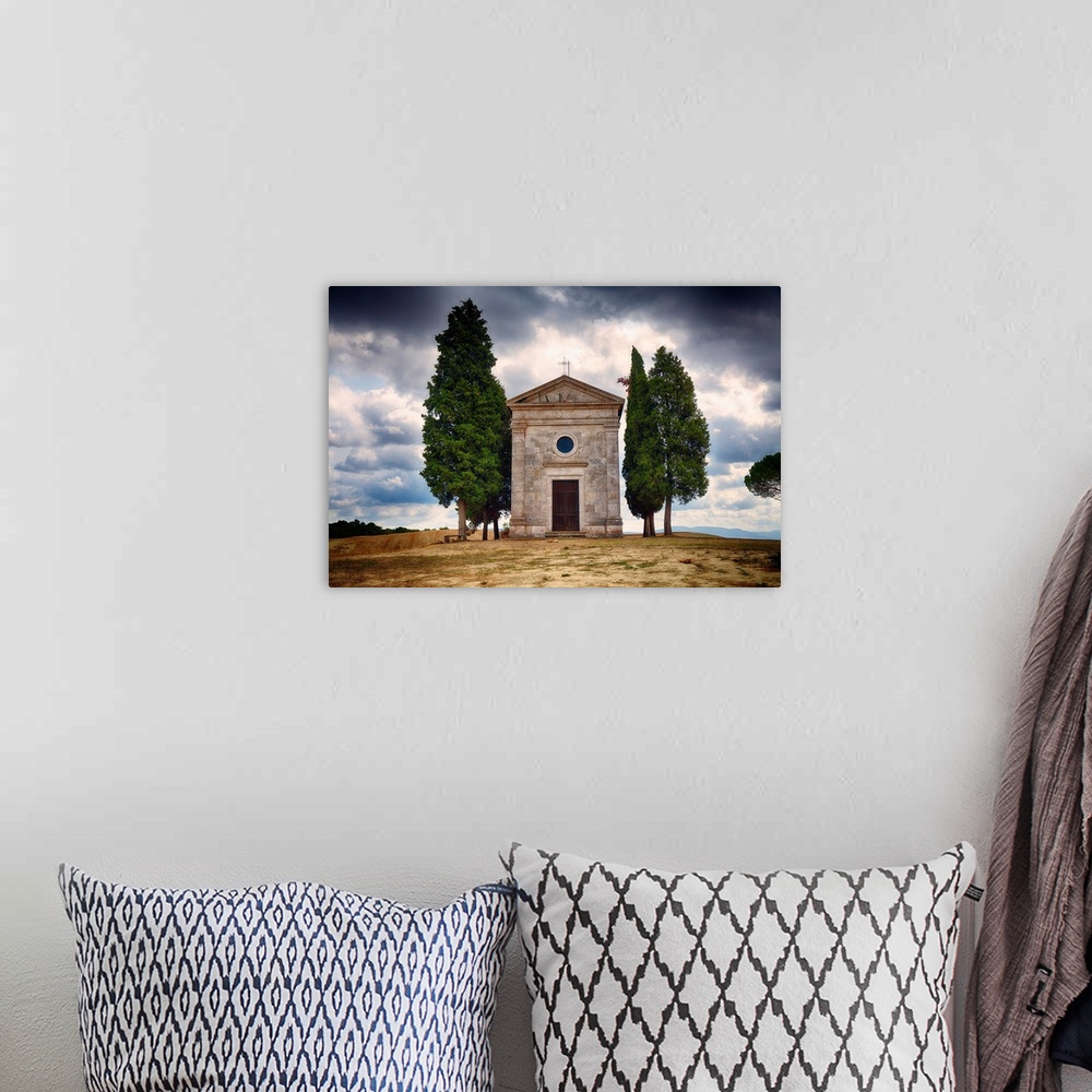 A bohemian room featuring A photograph of a small chapel with a backdrop of a Tuscan landscape against rolling clouds.